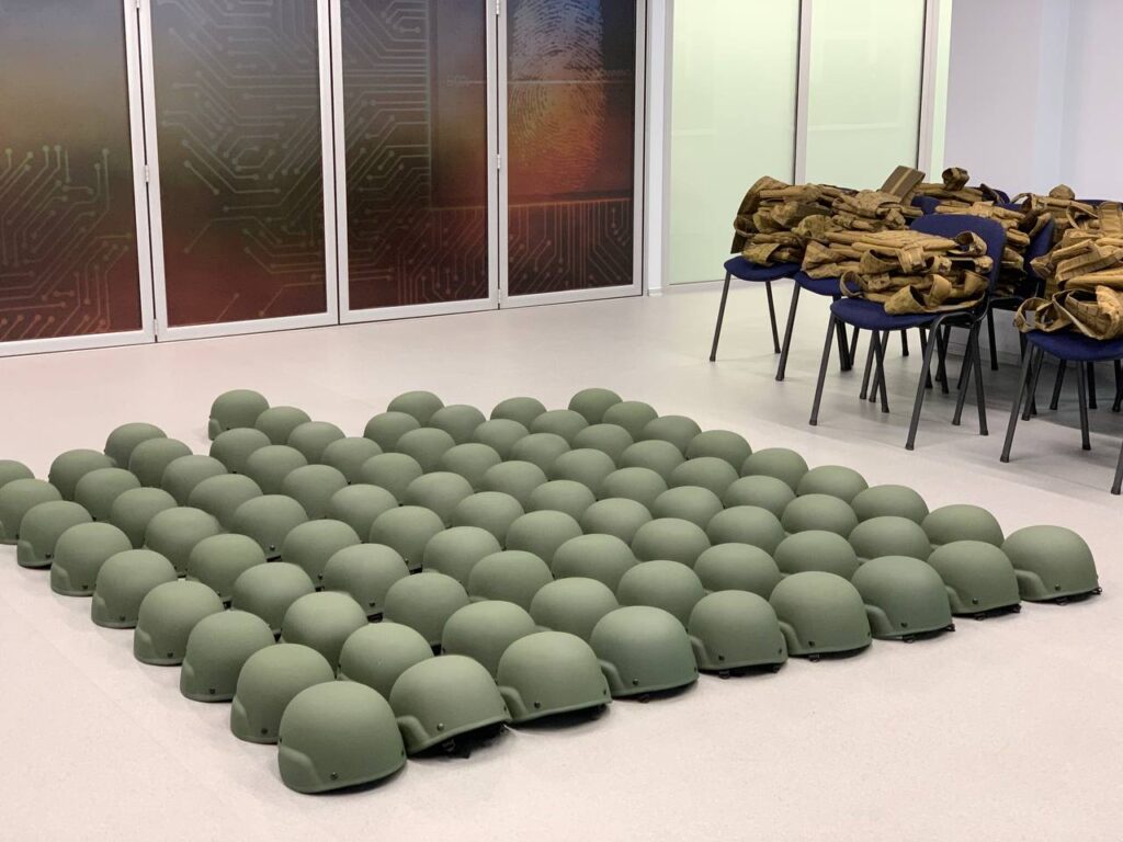 Ряди захисних шоломів на підлозі та спорядження на стільцях у приміщенні.