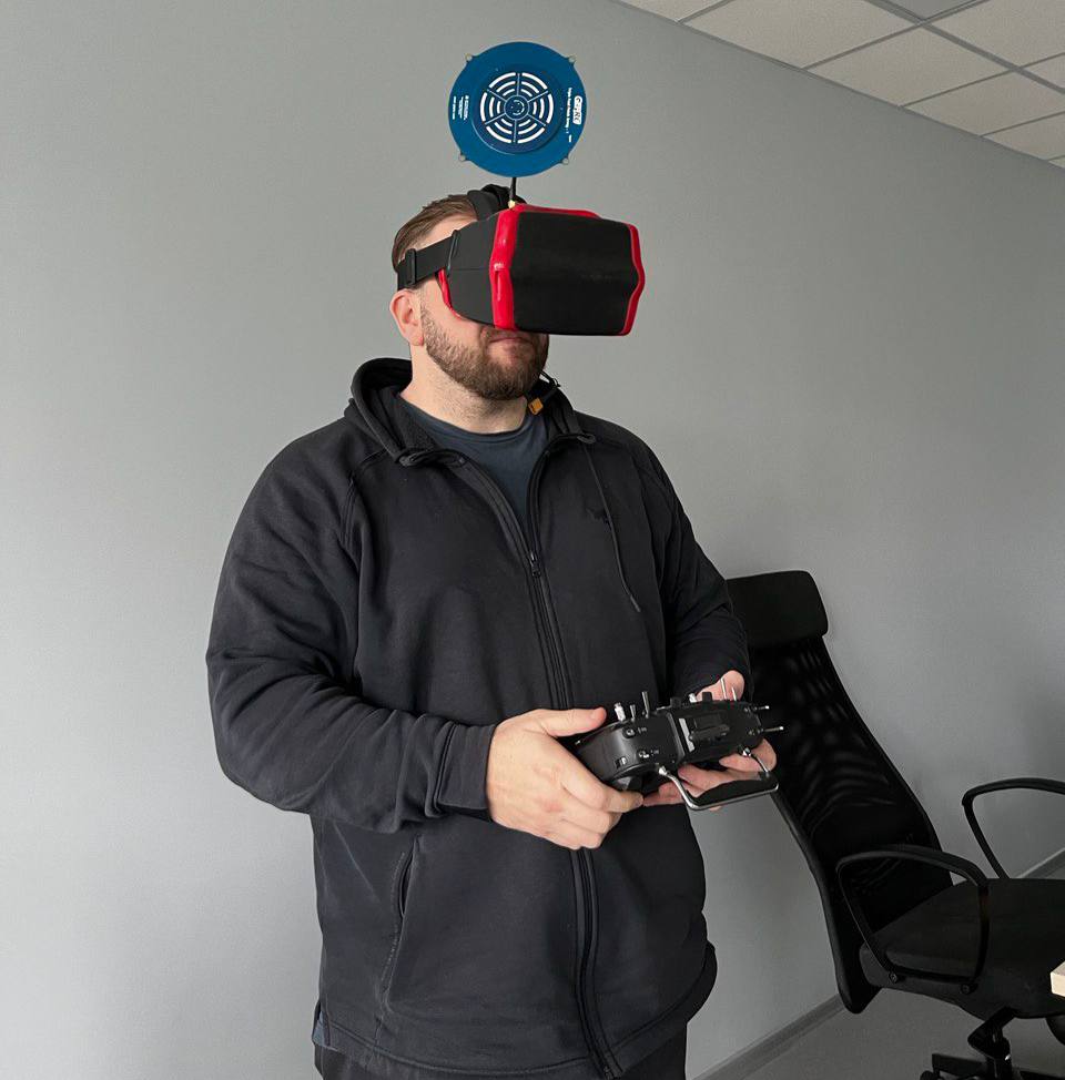 Людина в FPV-окулярах керує дроном з пультом під час тренування в школі FPV-пілотів.